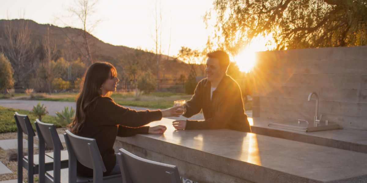 Couple sharing drinks at an outdoor bar with POLYWOOD bar chairs at sunset.
