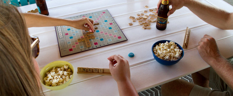 People playing the game Scrabble and enjoying snacks around a white POLYWOOD Farmhouse 37 Inch by 72 Inch Dining Table.