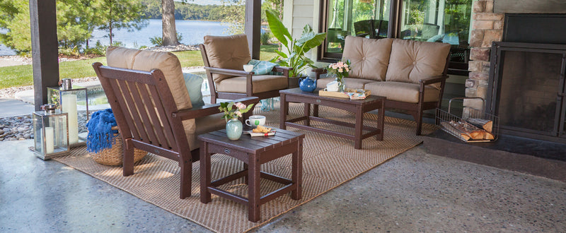 A brown POLYWOOD Vineyard 5-Piece Deep Seating Set with cream cushions on a patio overlooking a lake. Lanterns and a fireplace add to the cozy atmosphere.