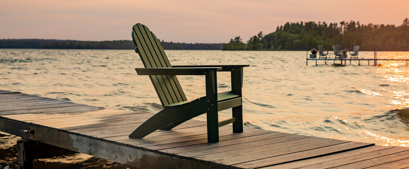 A POLYWOOD Vineyard Adirondack Chair in Green sits on a wooden pier overlooking a lake.
