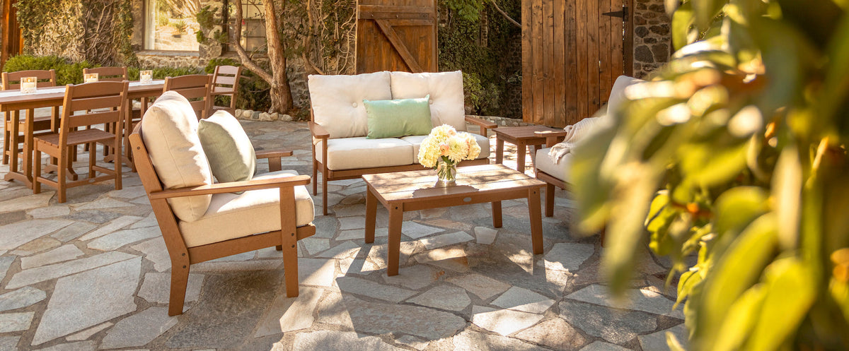 The POLYWOOD Lakeside Collection's deep seating and dining furniture in Teak are arranged on a stone patio.