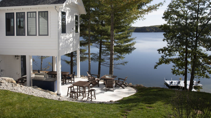 Assorted POLYWOOD furniture sits on a patio overlooking trees and a lake.
