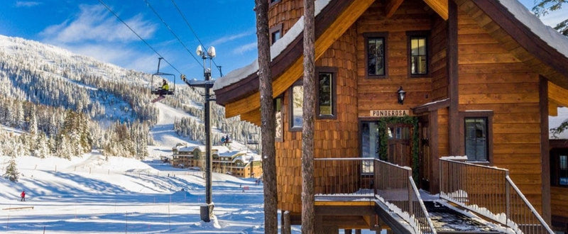 A cabin sits by a ski lift and a mountain covered in snow and evergreens.