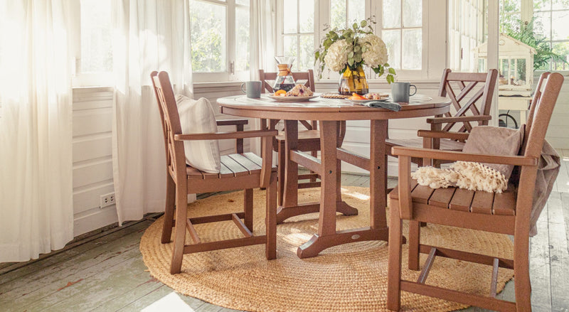 A POLYWOOD Chippendale 5 Piece Round Farmhouse Dining Set in Teak is set for a meal on a covered porch.
