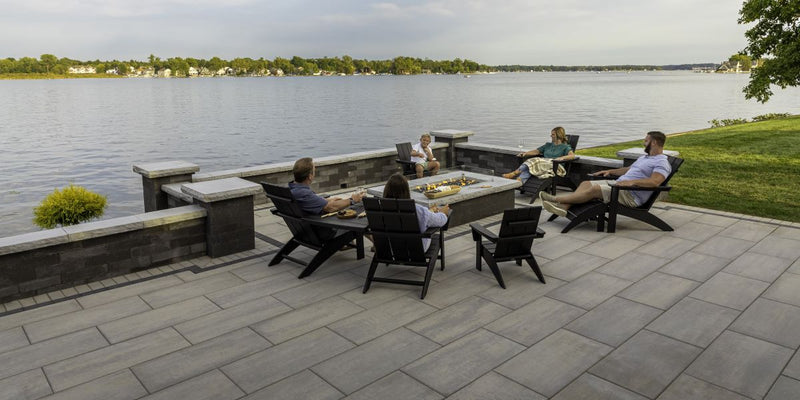 Group relaxing in black Adirondack chairs around a rectangular fire pit on a lakeside patio, ideal for modern outdoor entertaining.