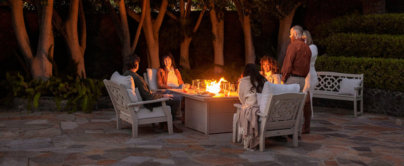 People sit and chat in POLYWOOD Chinoiserie Deep Seating Chairs by a Square 42 Inch Fire Pit Table on a stone patio at night.