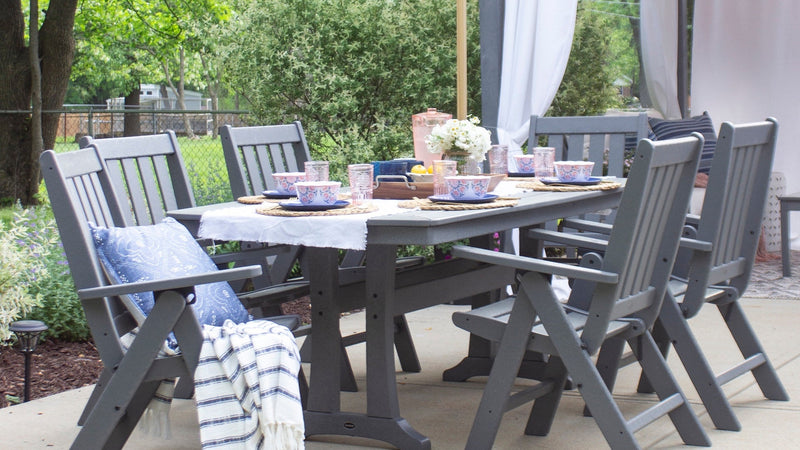 A grey POLYWOOD Vineyard Folding Chair 7 Piece Dining Set with Trestle Legs is set for a meal on a backyard patio.