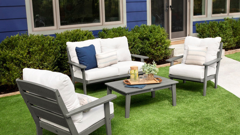 A POLYWOOD Lakeside 4 Piece Deep Seating Set in Slate Grey and Natural Linen is arranged on a green lawn before a blue house.