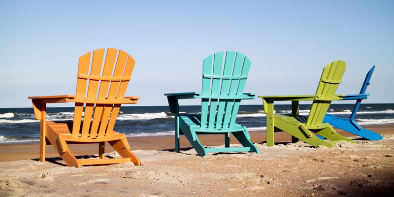 Colorful POLYWOOD Palm Coast Folding Adirondack chairs face the ocean on a sandy beach.