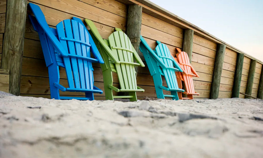 Colorful folding adirondack chairs leaned against a dune fence on a beach