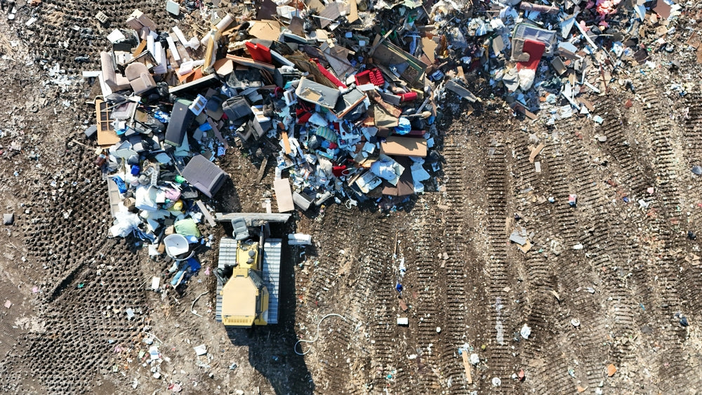 Aerial view of a landfill with discarded furniture and household waste being pushed by a bulldozer.
