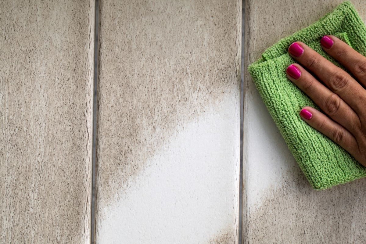 A hand with pink fingernails wiping down a white POLYWOOD outdoor bar cart with a green microfiber cloth, illustrating easy cleaning and maintenance.
