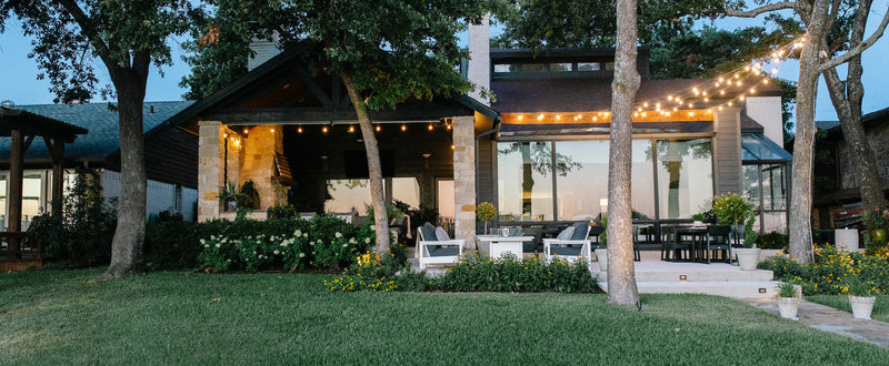 A backyard patio with outdoor furniture and string lights illuminated at dusk.