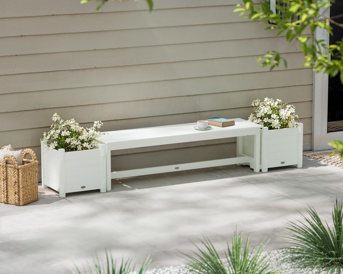 A white POLYWOOD 60-Inch Nautical Straight Planter Bench Set with white flowers sits by a beige wall on a concrete patio.