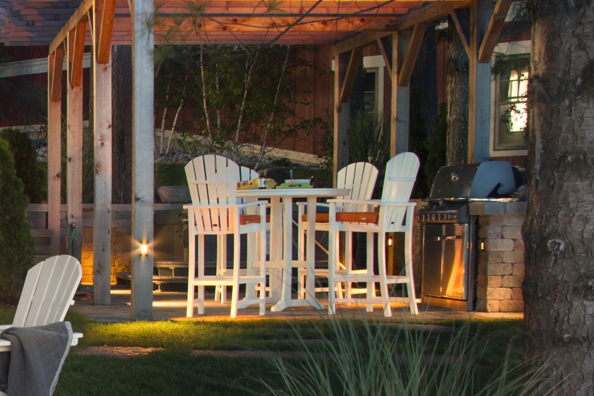 A White POLYWOOD Palm Coast 5 Piece Round Farmhouse Bar Set sits on a covered patio in the evening.