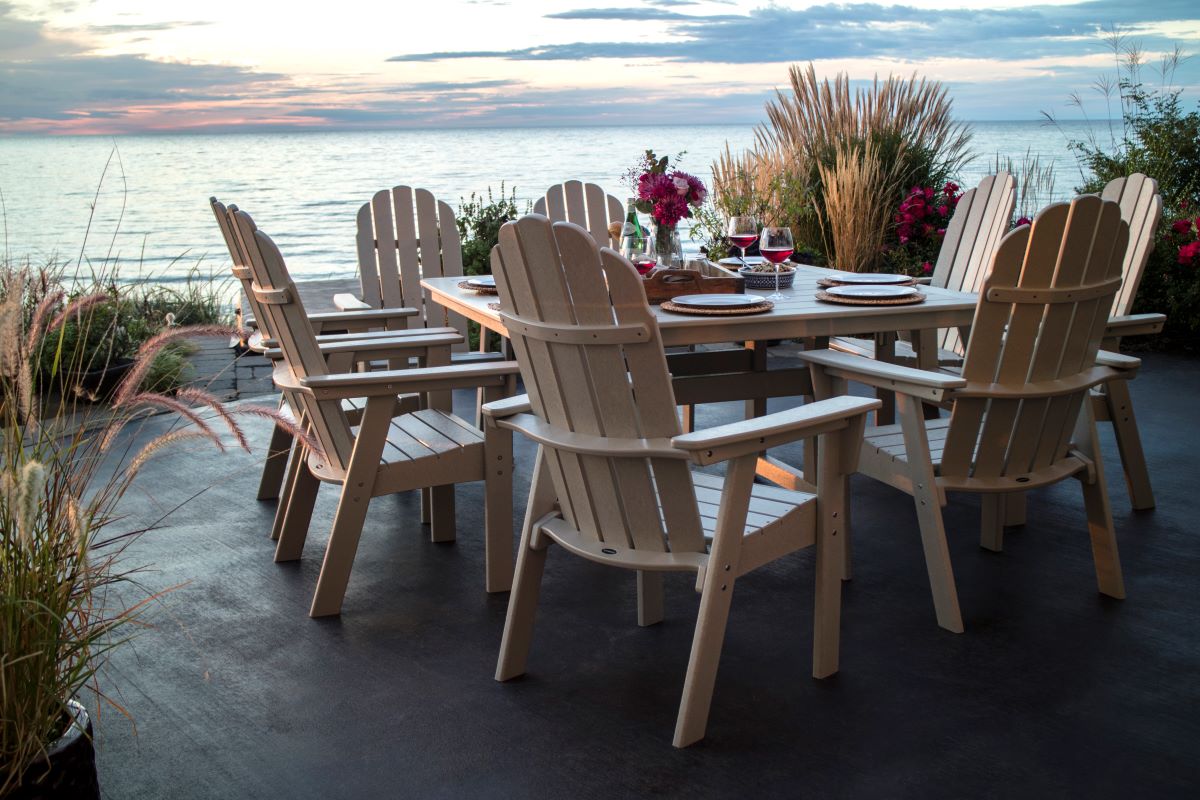 A white POLYWOOD outdoor dining set with six chairs on a patio overlooking the ocean at sunset, showcasing weather-resistant patio furniture ideal for coastal living.