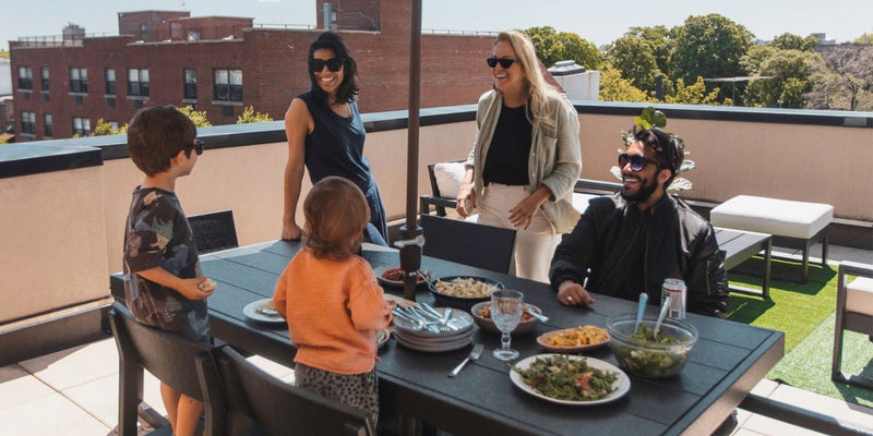 A family gathers for a meal around a black EDGE 7 Piece Dining Set on a rooftop terrace.