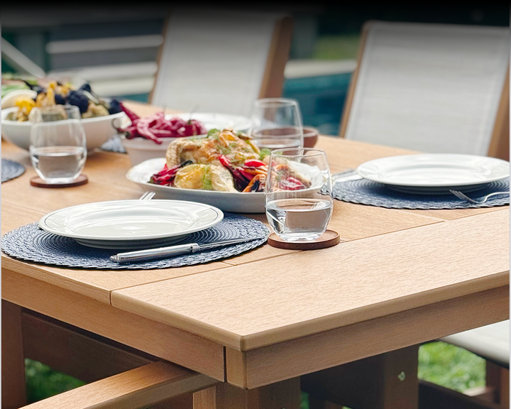 A brown POLYWOOD dining table is set with plates, glasses, and a plated meal beside dining chairs with white sling seats.