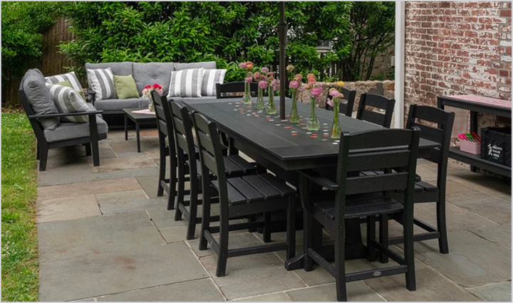 A black POLYWOOD dining set with vases of pink flowers and deep seating furniture with grey cushions sits on a stone patio.