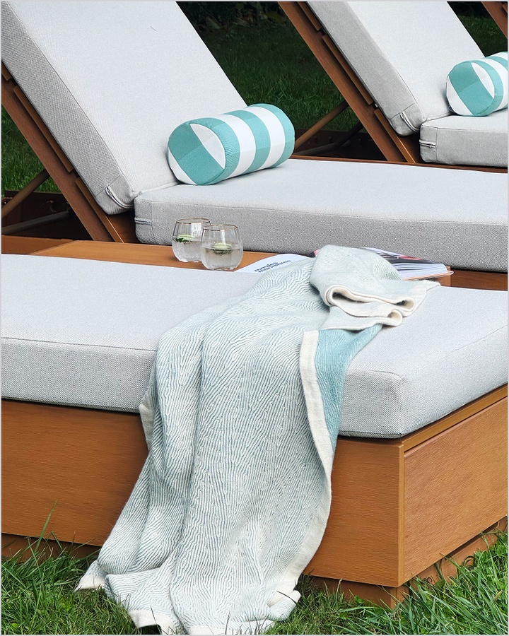 POLYWOOD chaise lounges with white cushions and striped pillows sit in a grassy area with a throw blanket and drinks.