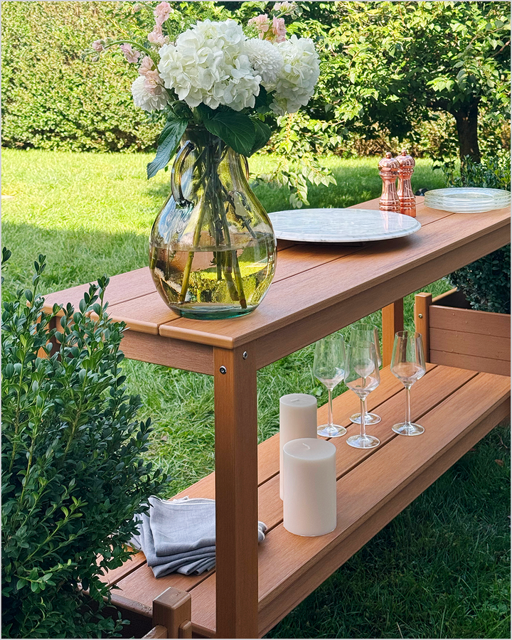 A brown POLYWOOD Newport 55-Inch Console Table displays flowers, plates, wine glasses, and candles in an outdoor setting.